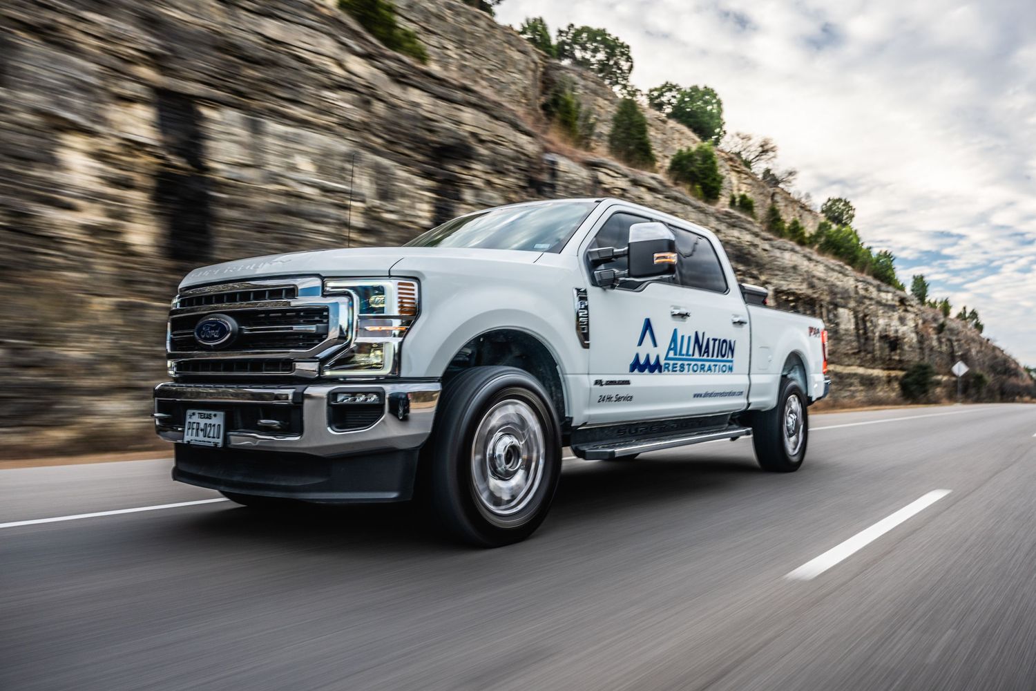 A silver Ford pickup truck driving past rocky cliffs on a mountain road.