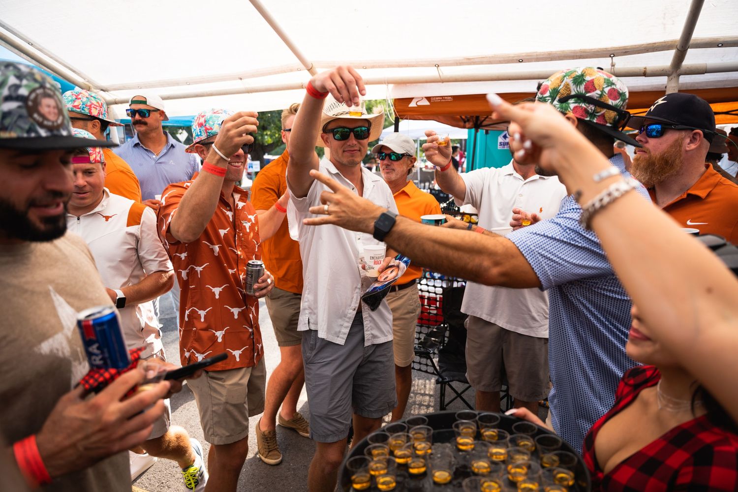 Partygoers cheering and celebrating with drinks under a white tent.