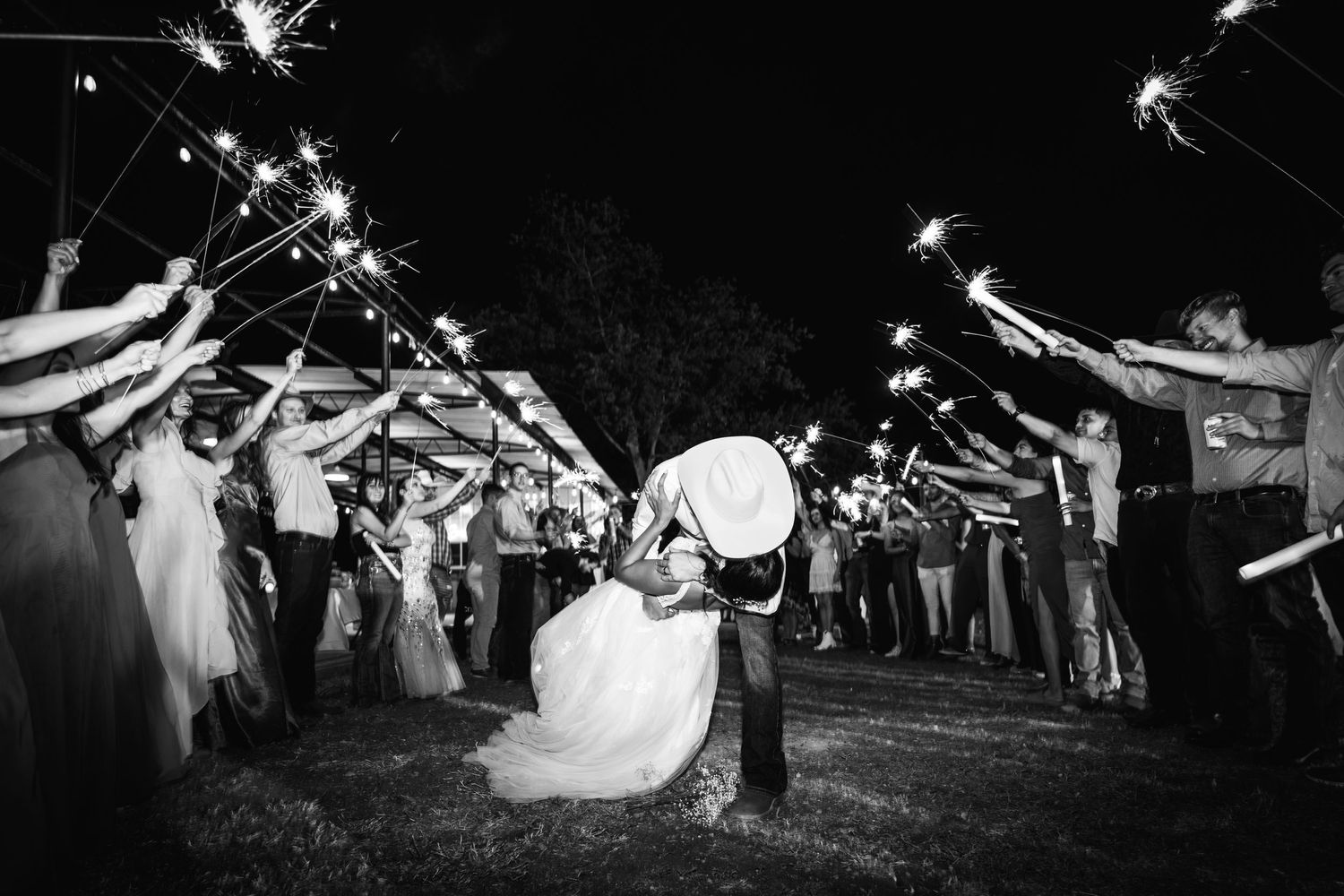 Wedding couple dips under sparkler exit tunnel created by guests at nighttime.