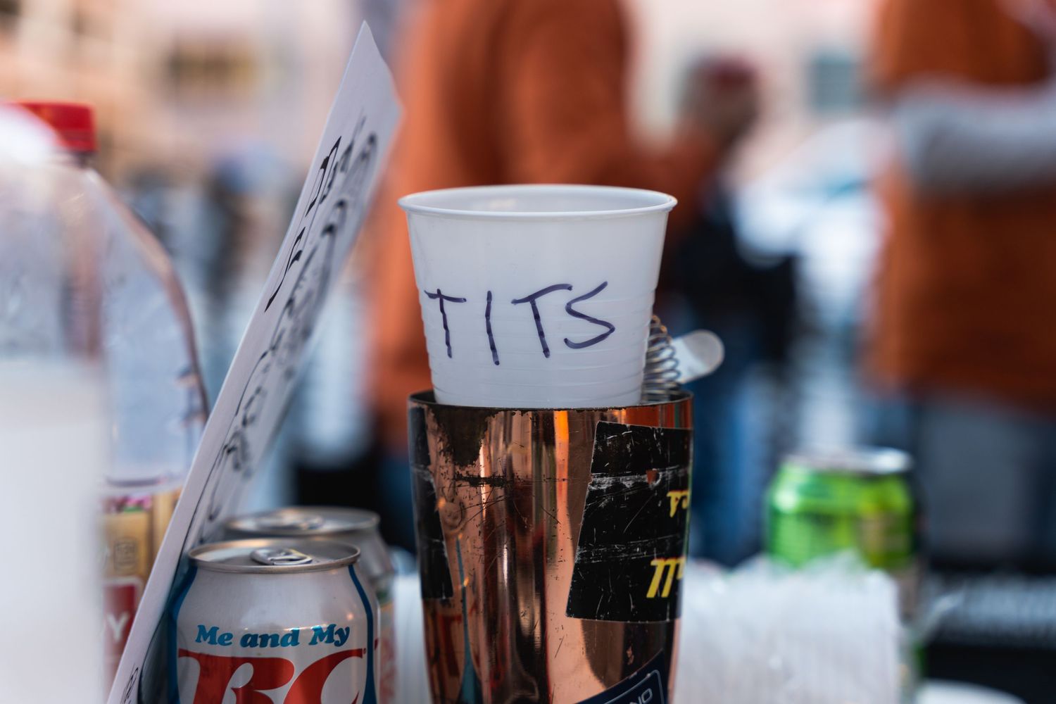Close-up shot of a labeled clear plastic cup containing beer at an outdoor event.