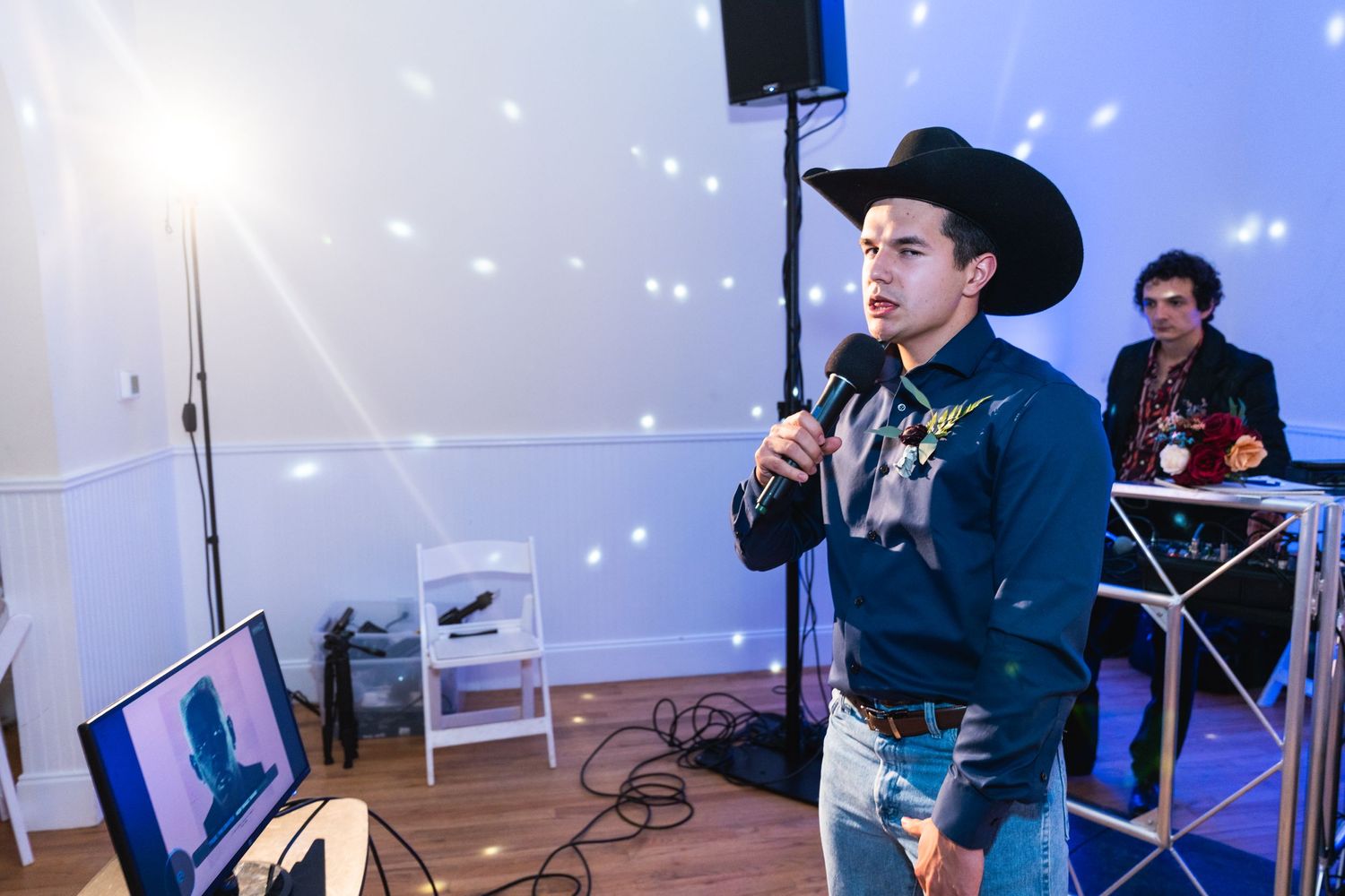 A performer in western attire sings into a microphone with glowing lights in the background.