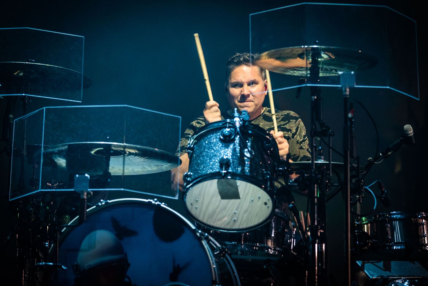 Drummer performs with intensity behind blue-lit drum kit on concert stage.