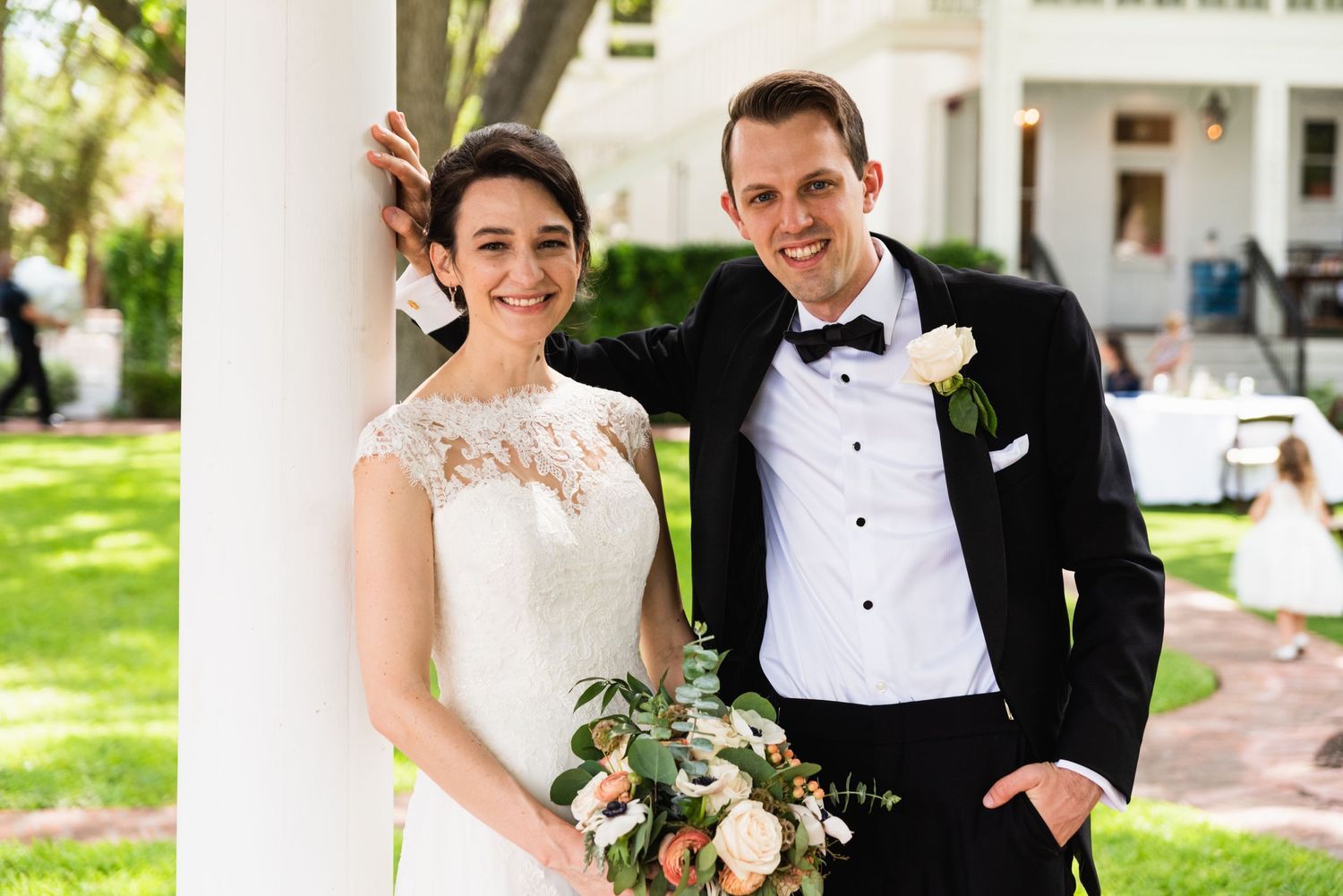 An elegant wedding portrait on a white columned porch with a garden backdrop.