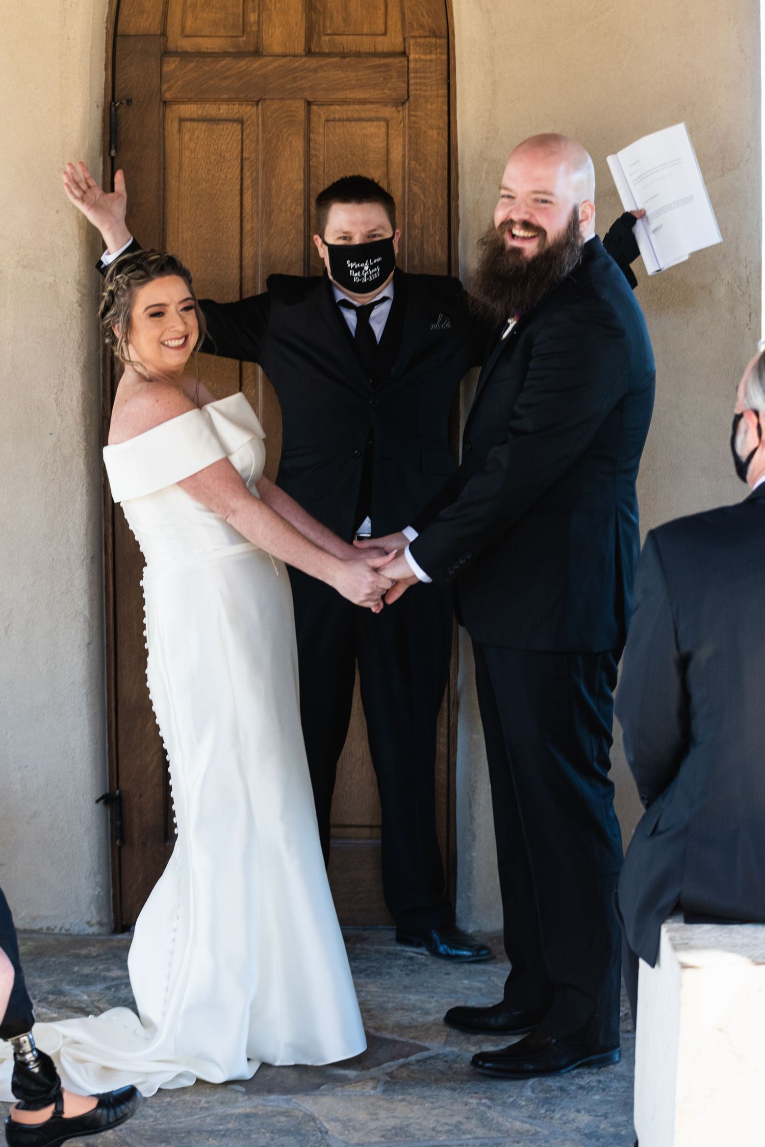 A wedding ceremony in front of a wooden door with the couple and officiant in formal attire.