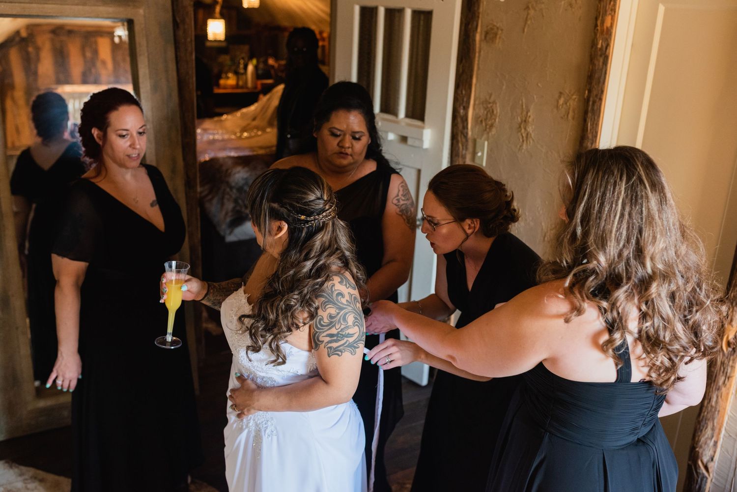 A group helps prepare a bride in a dimly lit rustic room.