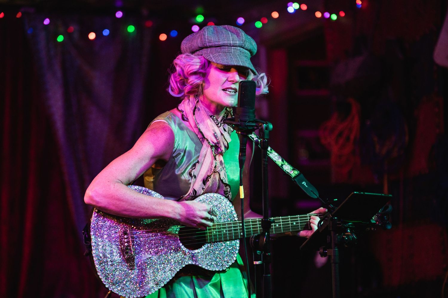 A musician performs with a sparkly guitar under colorful stage lighting at a club venue.