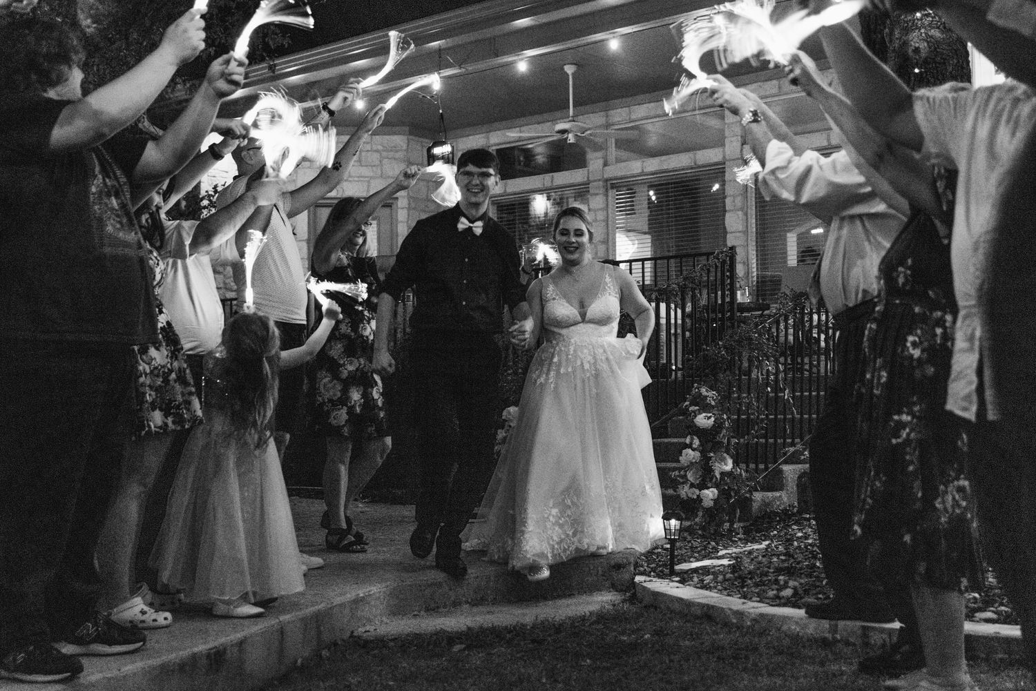 Wedding guests create a sparkler tunnel exit for the newlyweds in black and white photography.