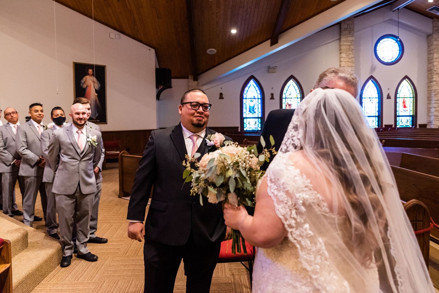 Wedding ceremony moment in church with groomsmen in grey suits watching.