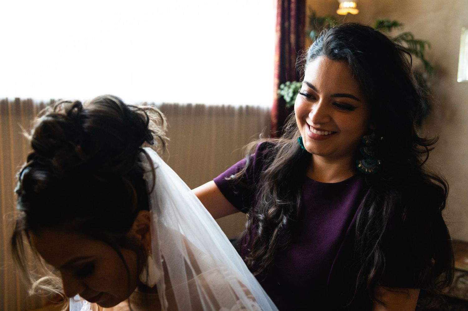 Two people share a joyful moment during wedding preparations in a sunlit room.