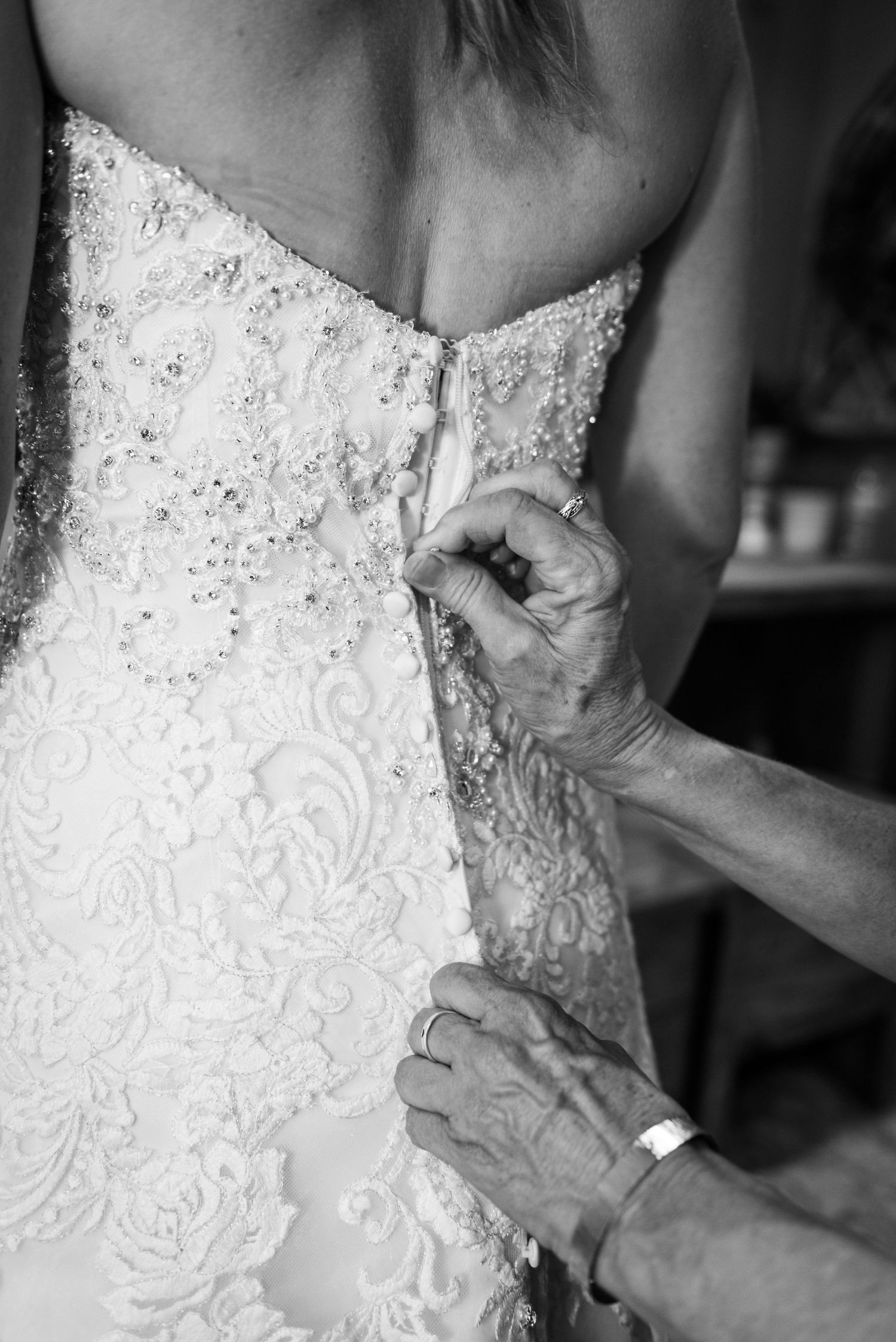 Close-up black and white shot of intricate lace details being adjusted on a wedding dress.