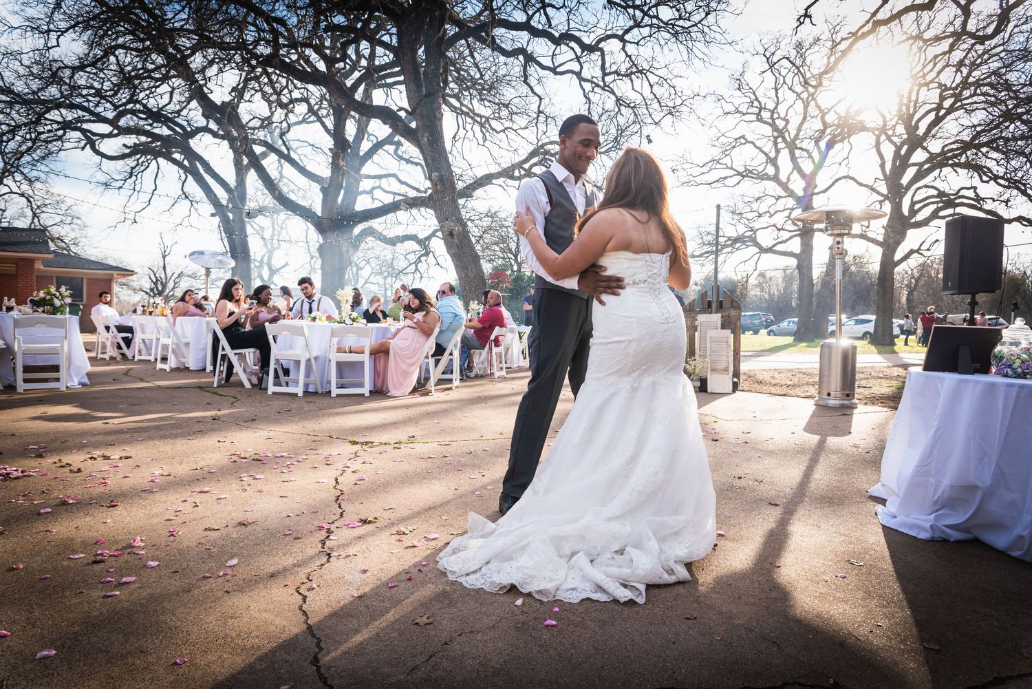 Newlyweds share romantic dance at outdoor reception with string lights and guest tables.
