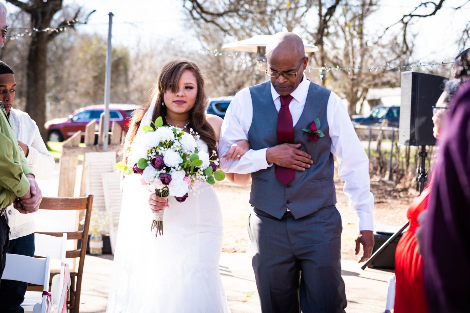 A couple walks down the aisle at an outdoor ceremony with the bride holding a white floral bouquet.