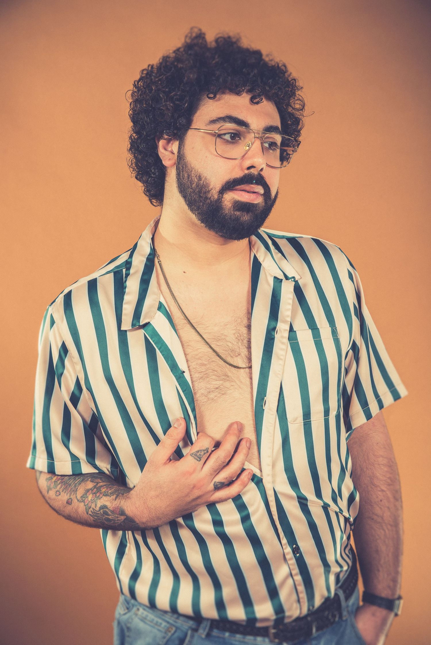 Dramatic portrait of person in striped shirt with hand on chest against orange backdrop.