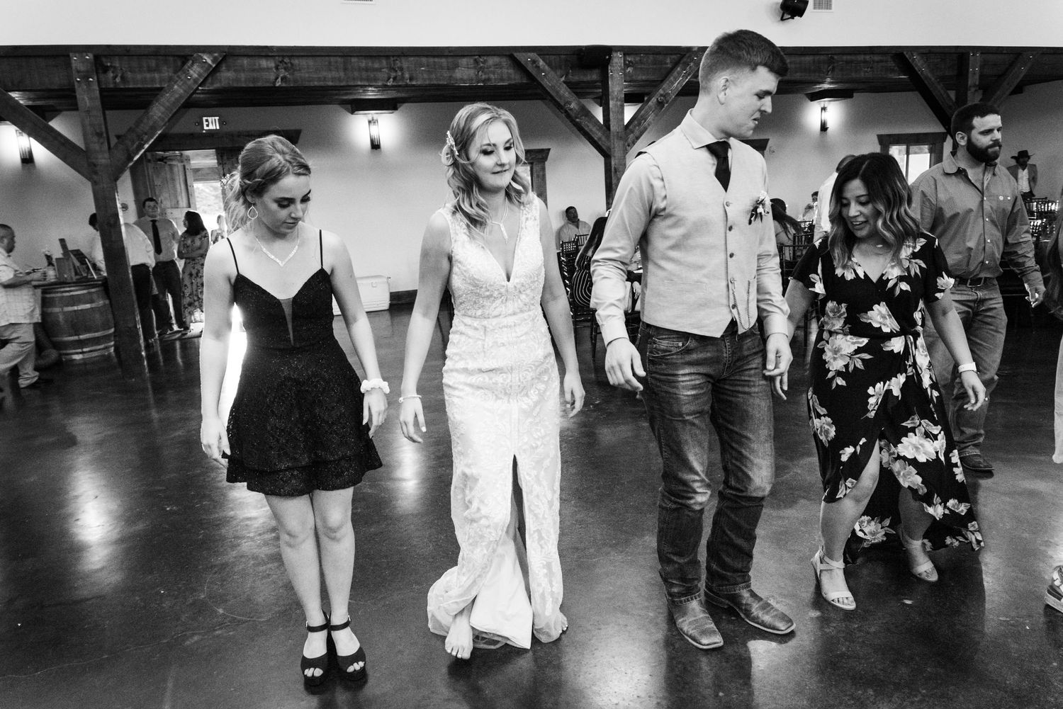 Black and white photo of wedding guests dancing together on a polished reception venue floor.