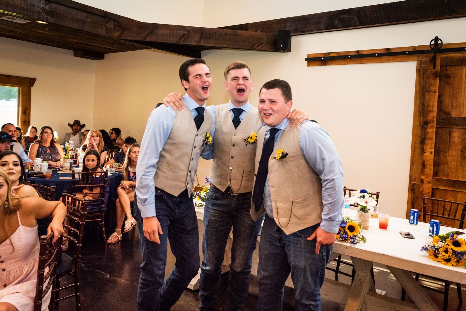 Groomsmen in matching vests sing enthusiastically during wedding reception festivities.