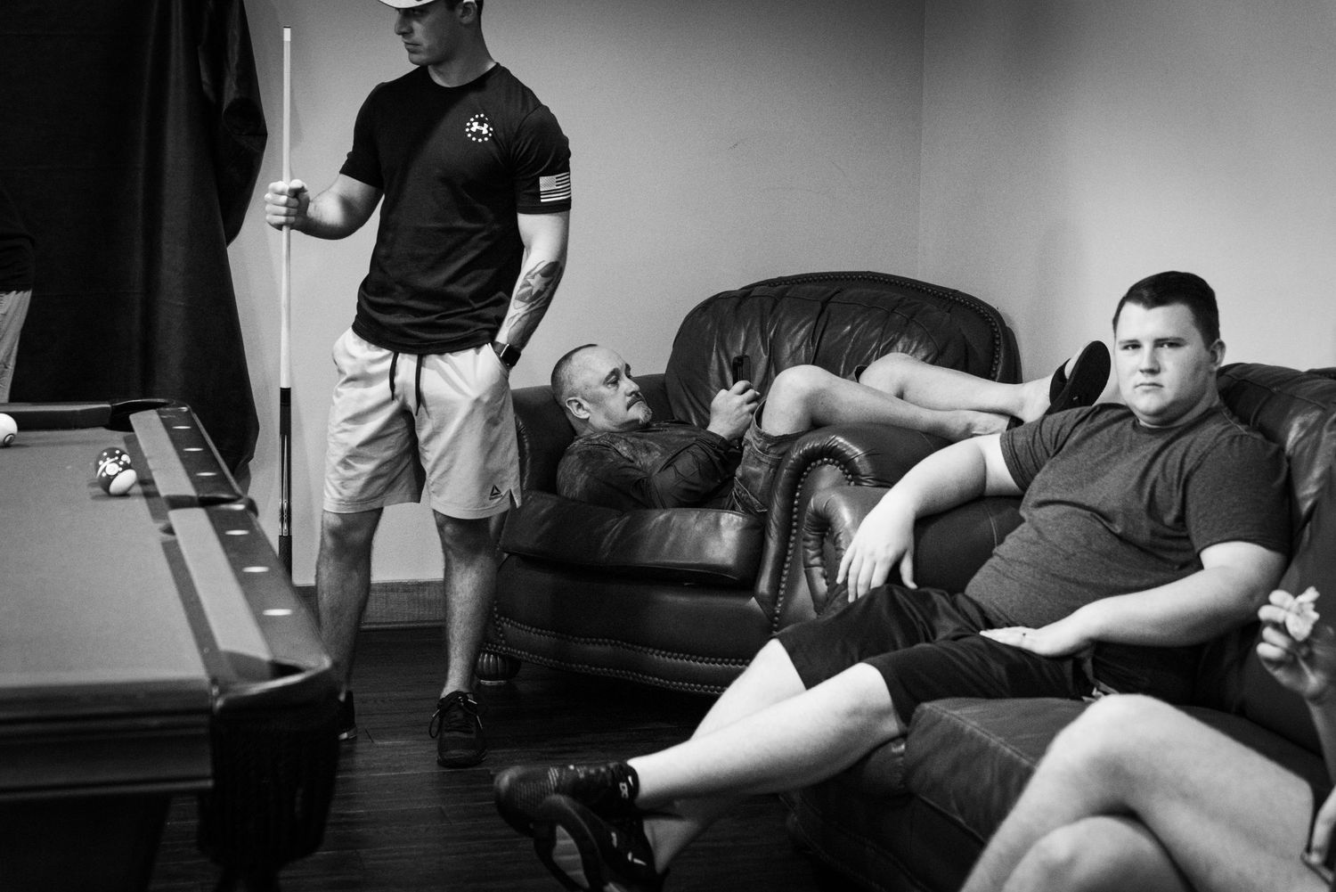 Three people relaxing in casual setting with pool table in background.