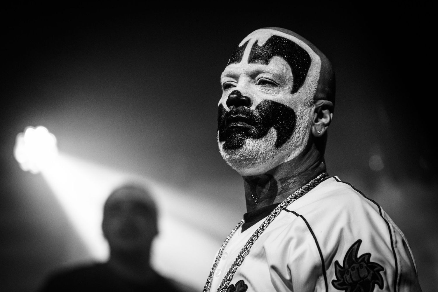 Black and white portrait of performer in distinctive face paint under bright stage lighting.