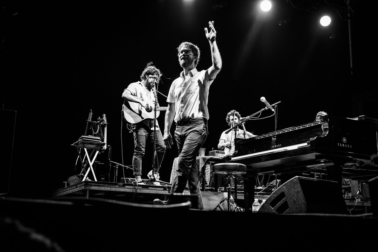Musicians performing on stage during a concert with dramatic lighting and raised hands.