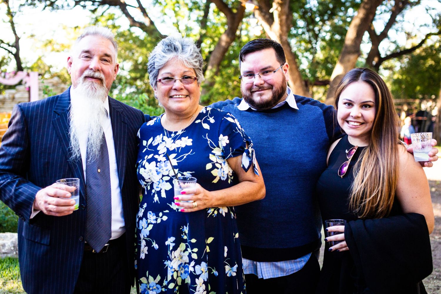 A group of wedding guests smile together at an outdoor reception.