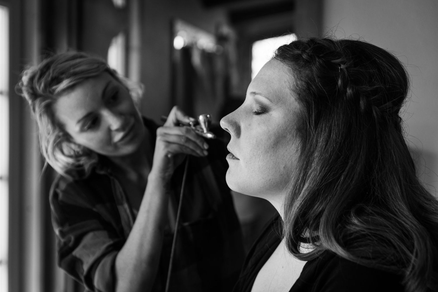 A makeup artist applies cosmetics in dramatic black and white lighting.