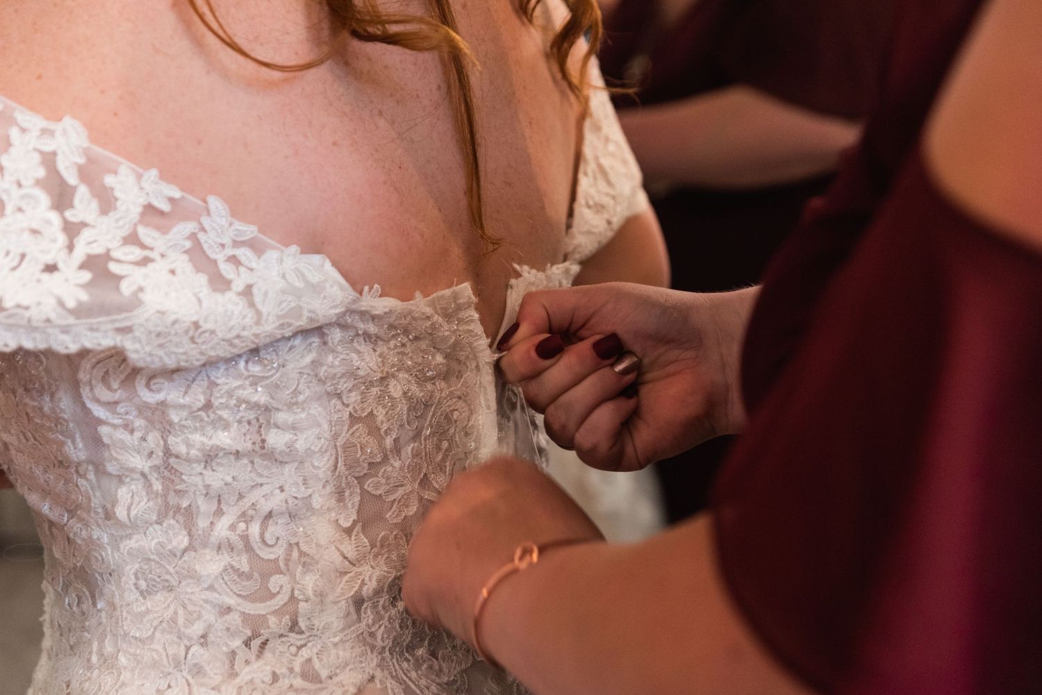 Detail shot of hands adjusting the back of an ornate lace wedding dress.