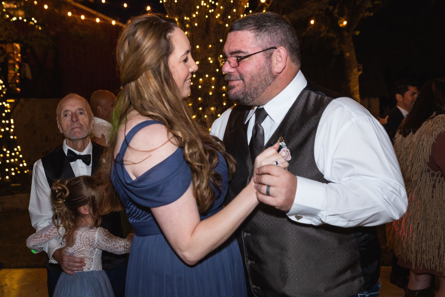 Wedding guests dancing together under twinkling lights at an evening reception.