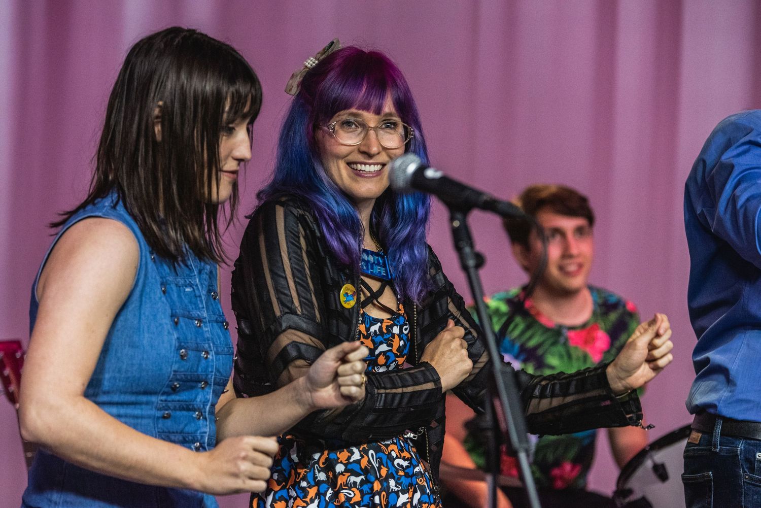 Musicians performing together on stage with pink curtain backdrop.