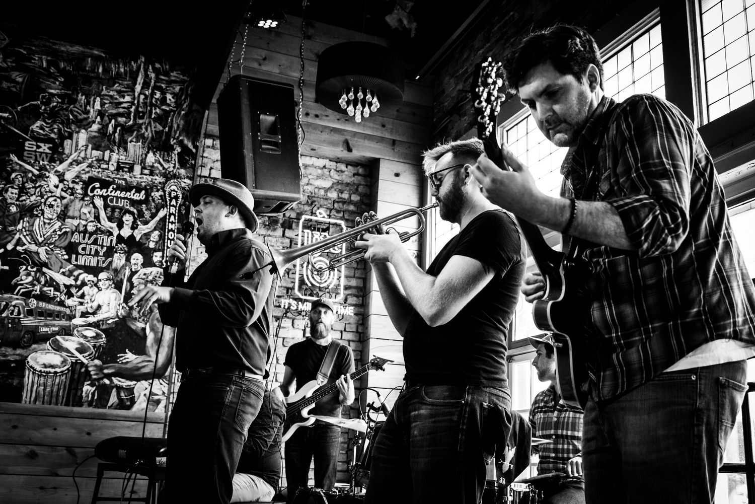 Musicians performing in dynamic black and white composition with instruments against textured wall.