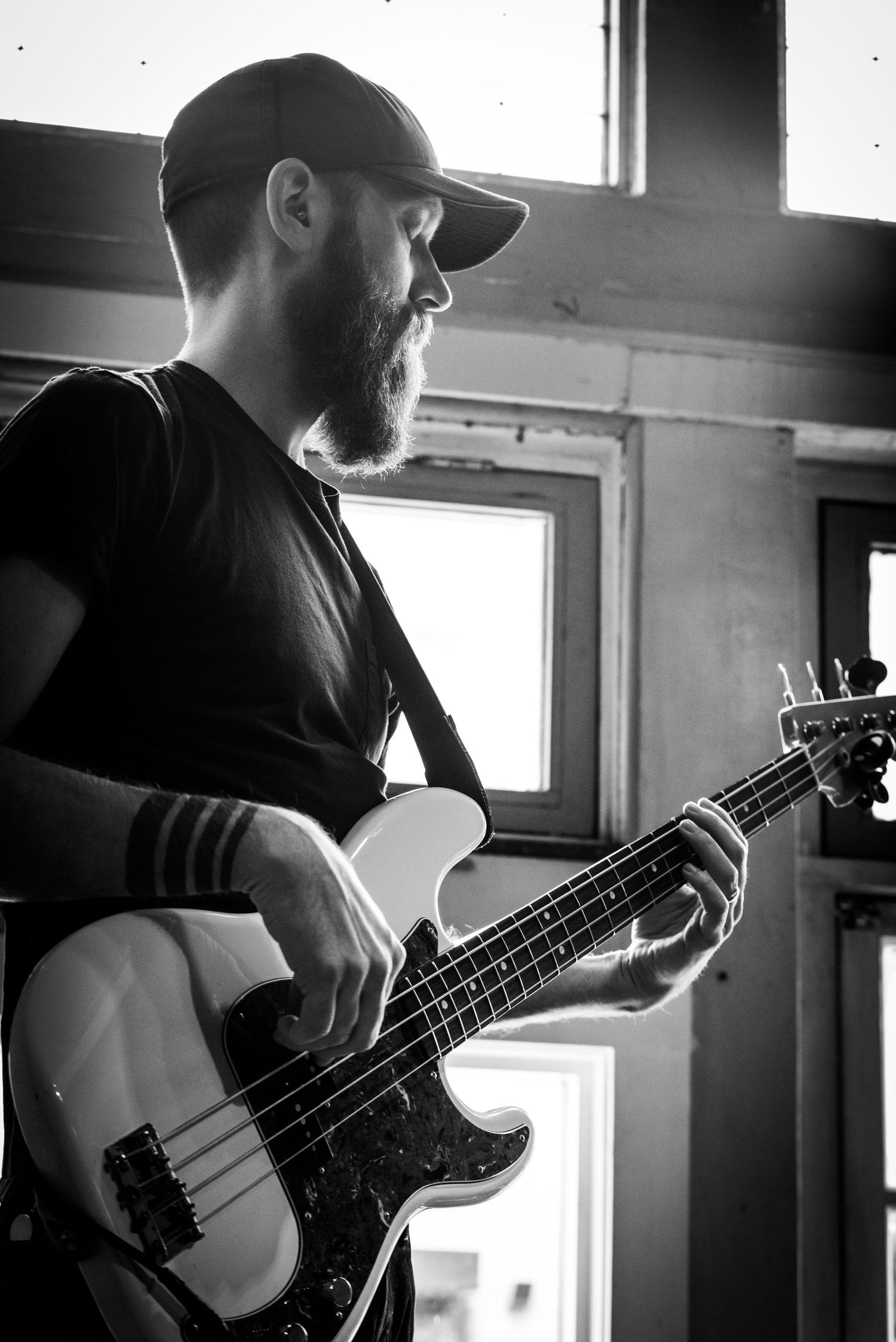 A bass player performing with a white electric bass guitar near a window.