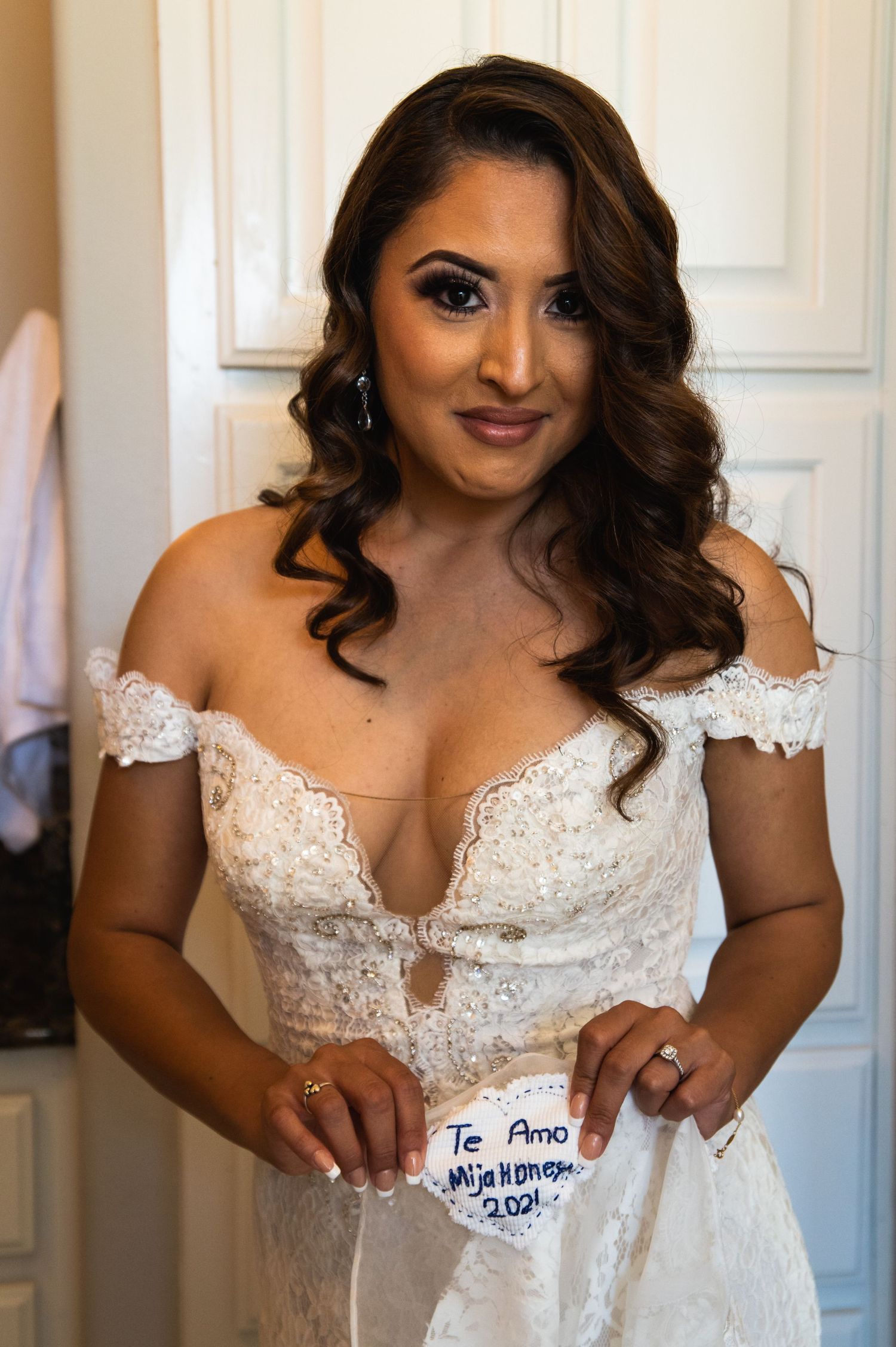 Beautiful bride in white lace off-shoulder wedding dress with glamorous makeup and curled hair.