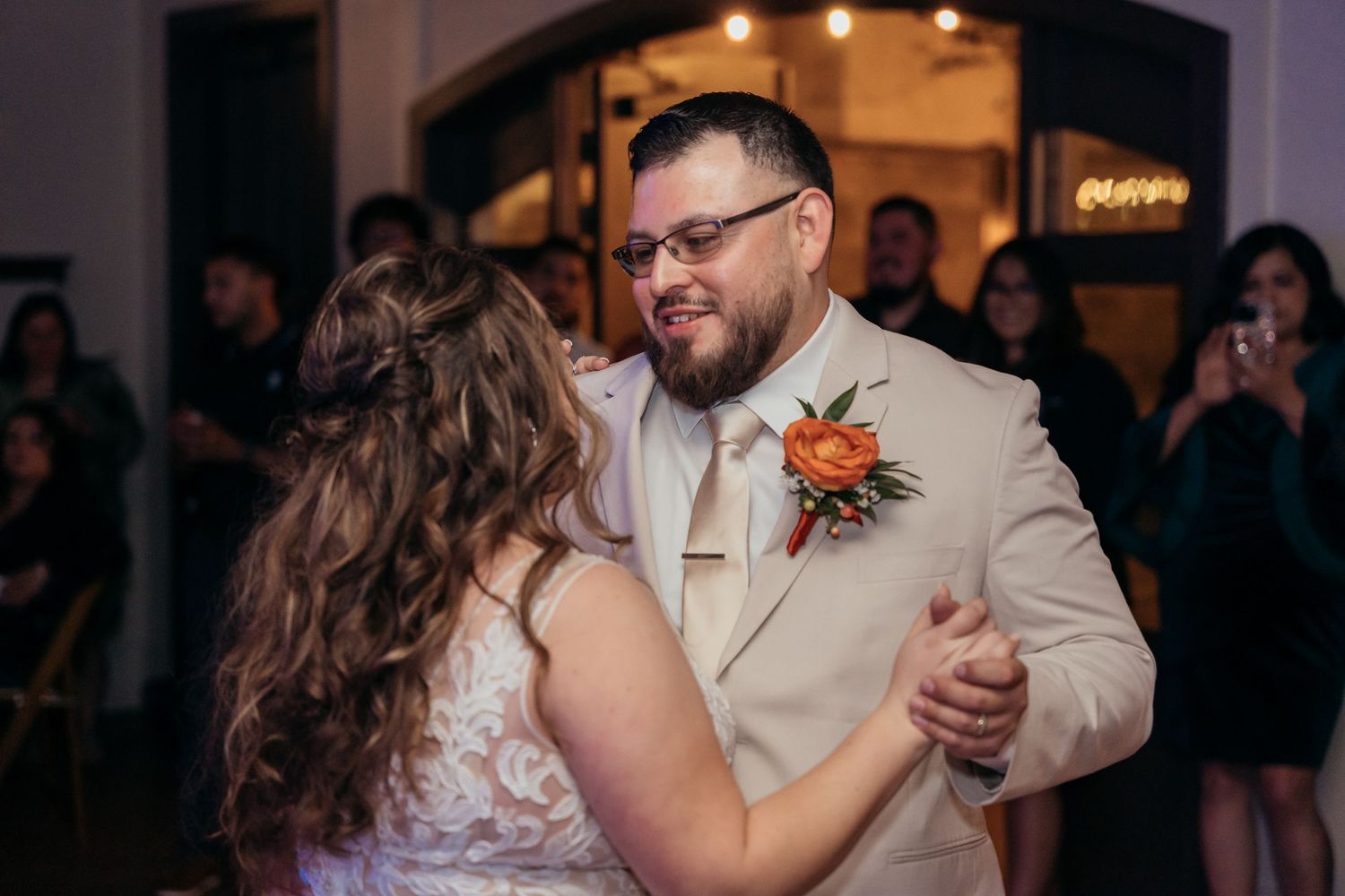 A couple shares their first dance at a wedding reception under warm lighting.