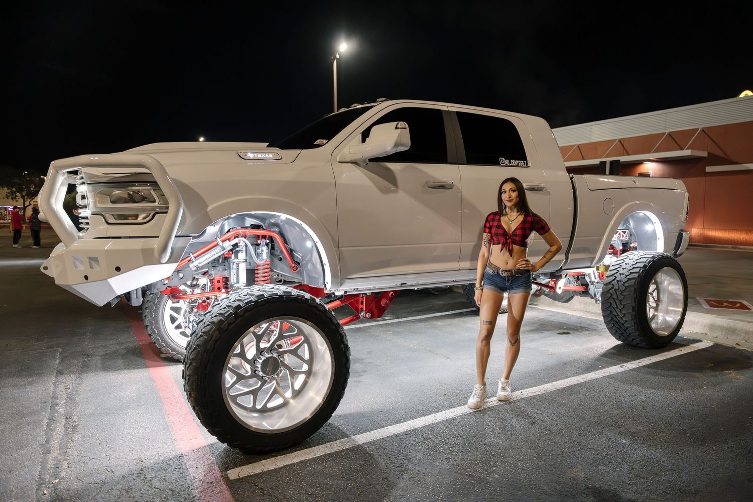 White lifted RAM truck with custom suspension and illuminated wheels at night.