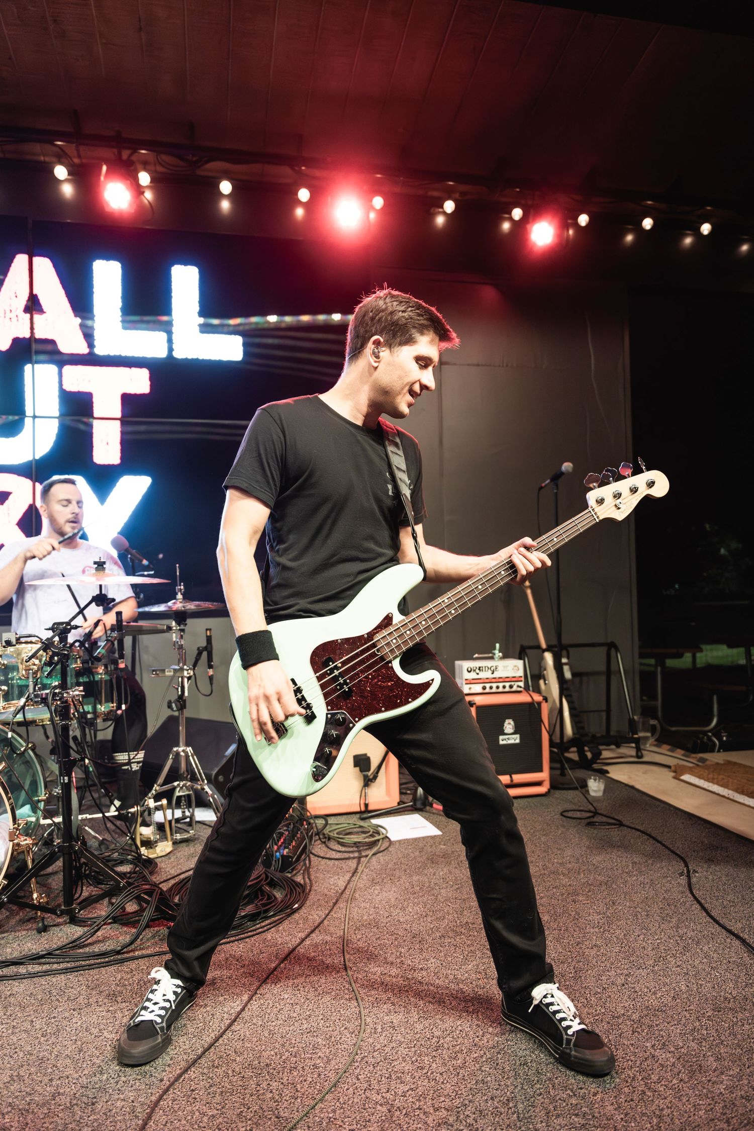 Bass player performing on stage with Y'ALL OUT BOY sign illuminated in background.