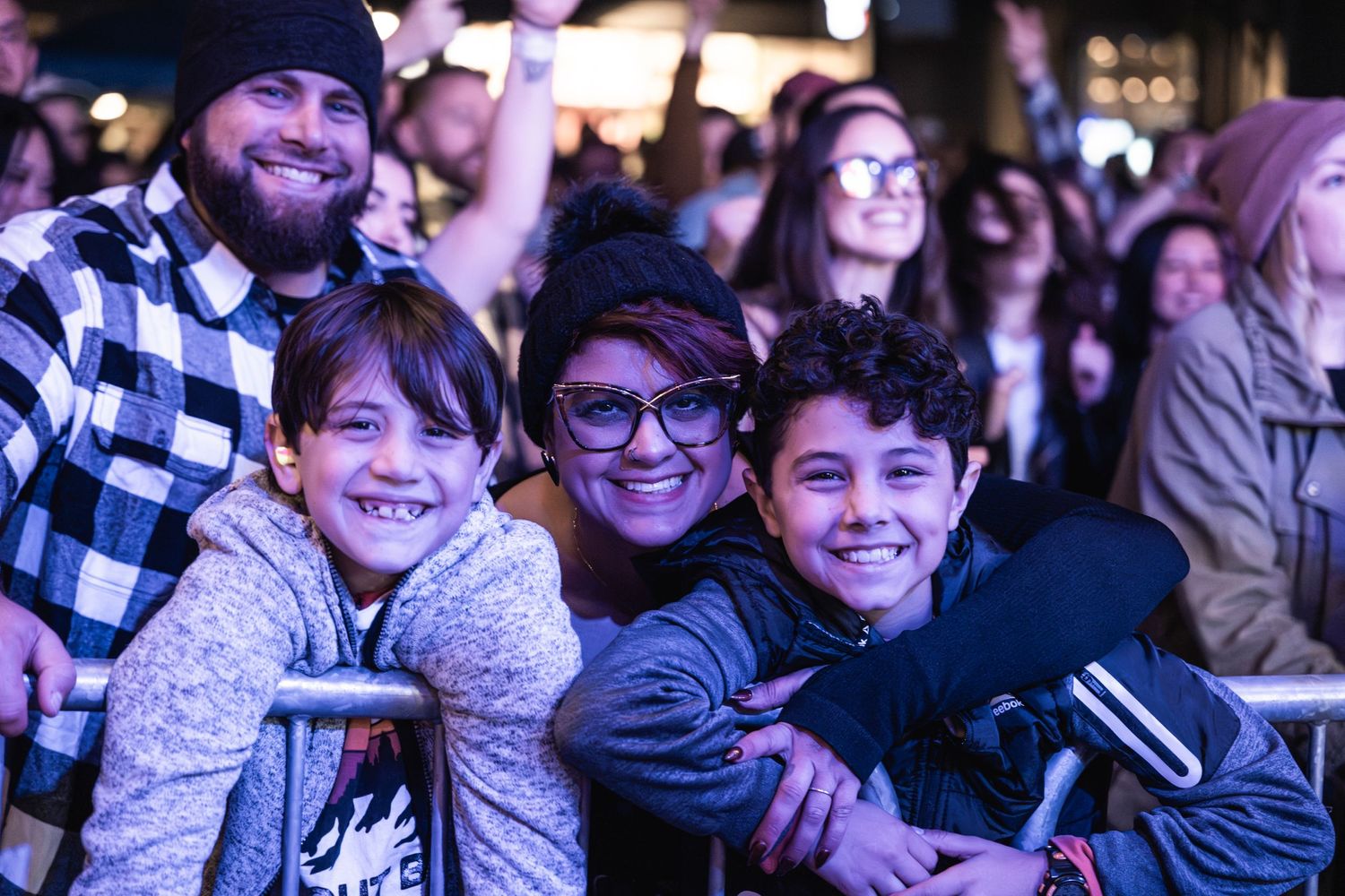 Group of young fans enjoying themselves at a concert with colorful lighting.