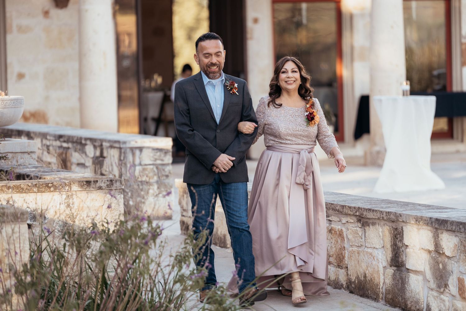 Couple stands together outdoors by stone wall at wedding venue in formal attire.