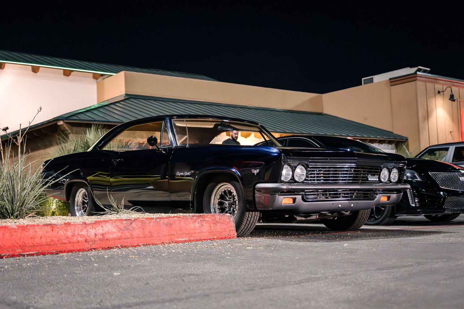 Classic black muscle car parked outside a building at night.