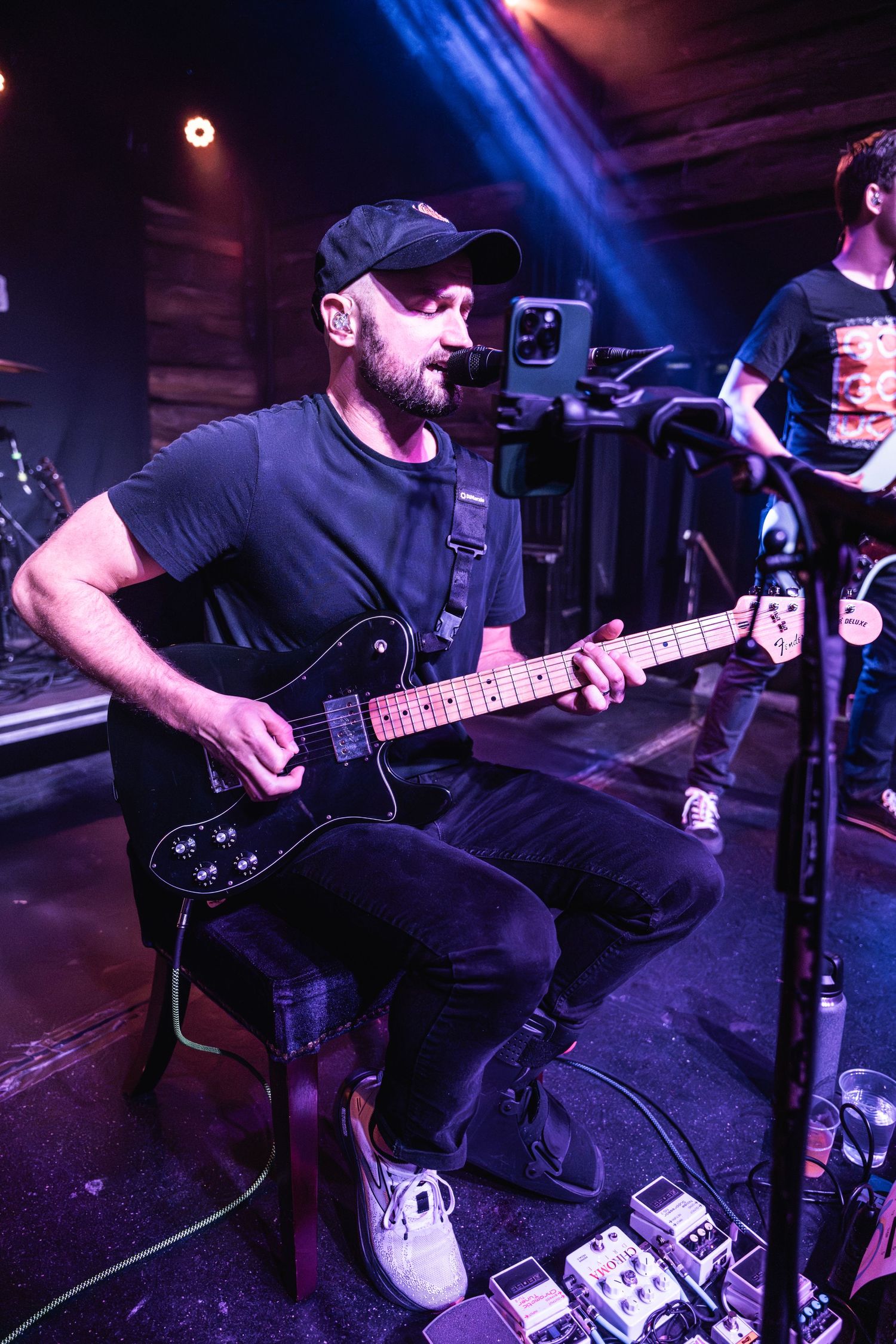 Guitar player performing on stage with pedal board and blue stage lighting.