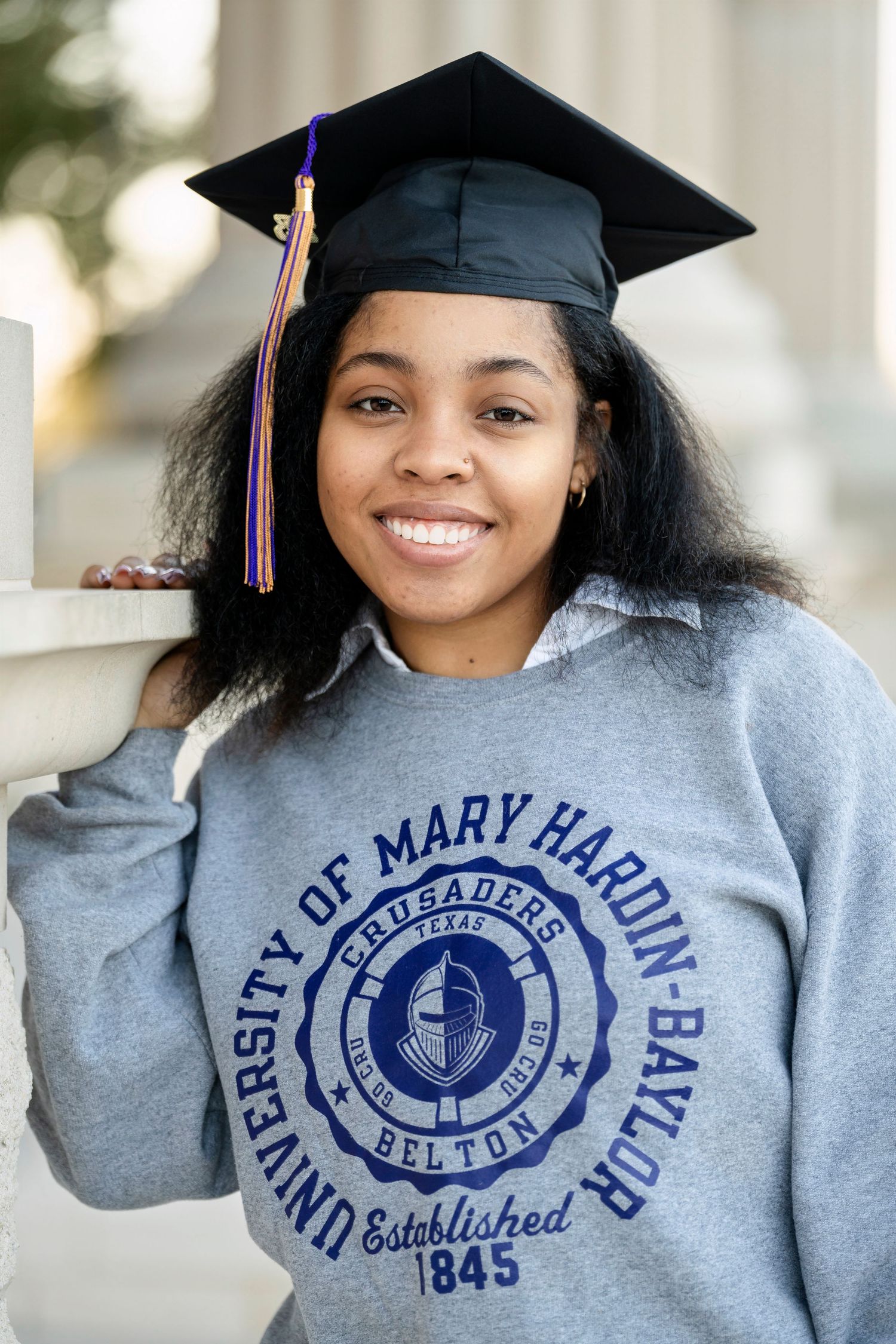 A close-up graduation photo showcasing a University of Mary Hardin Baylor sweatshirt with established 1845 seal.