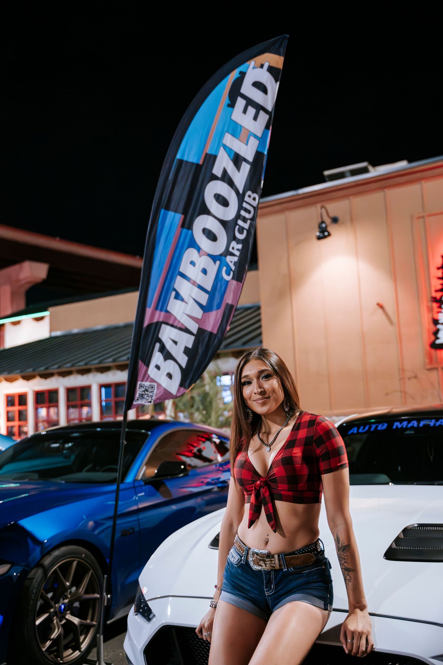Person in red plaid top poses next to white Audi with Mazzoledi banner in background.