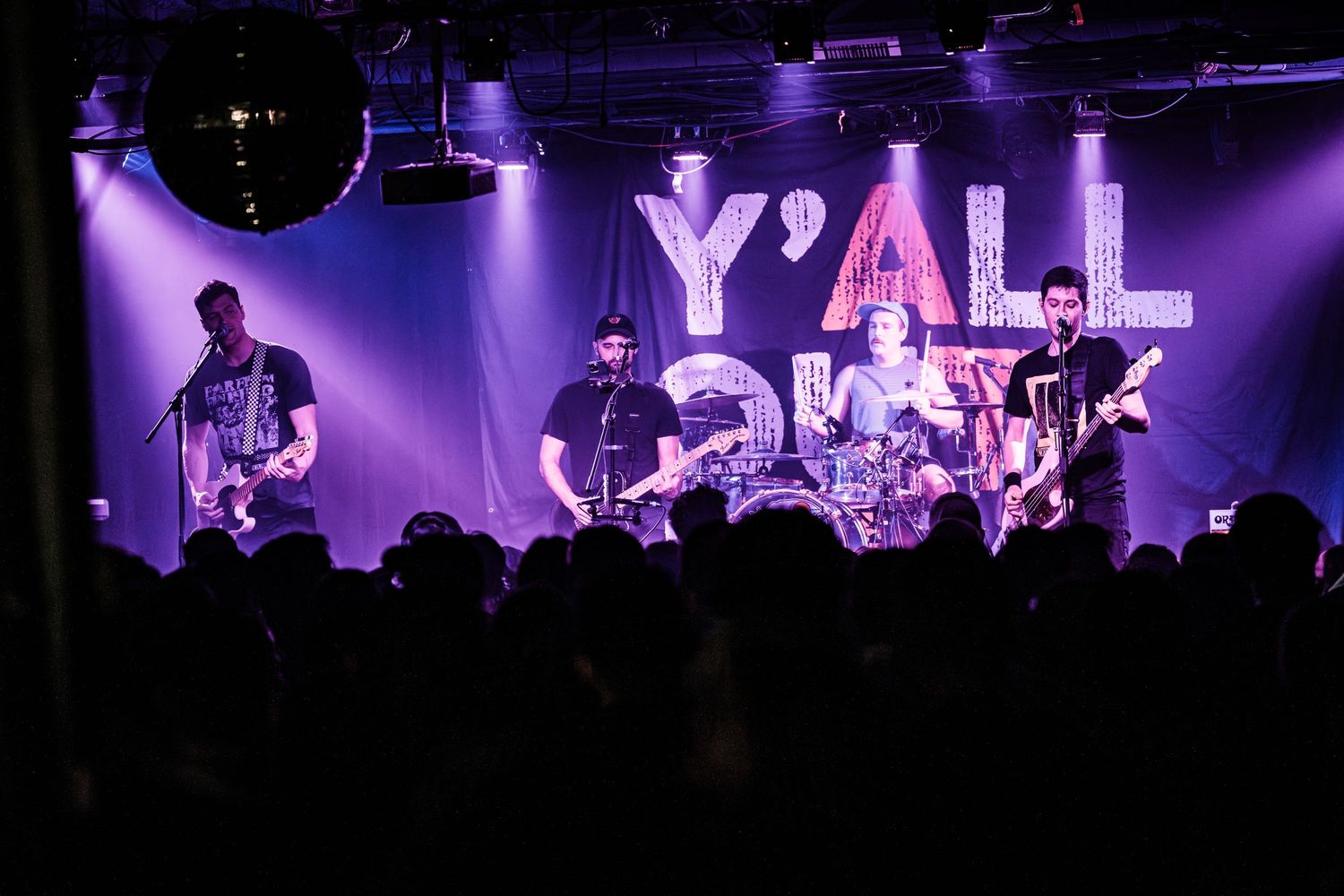 Band performing on stage with 'Y'ALL' text displayed in large letters behind them.