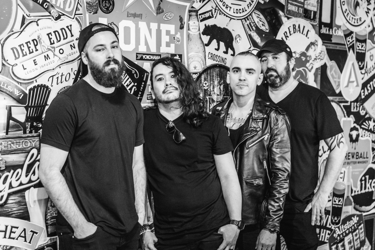 Black and white photo of a rock band posing against a wall covered in music posters and artwork.