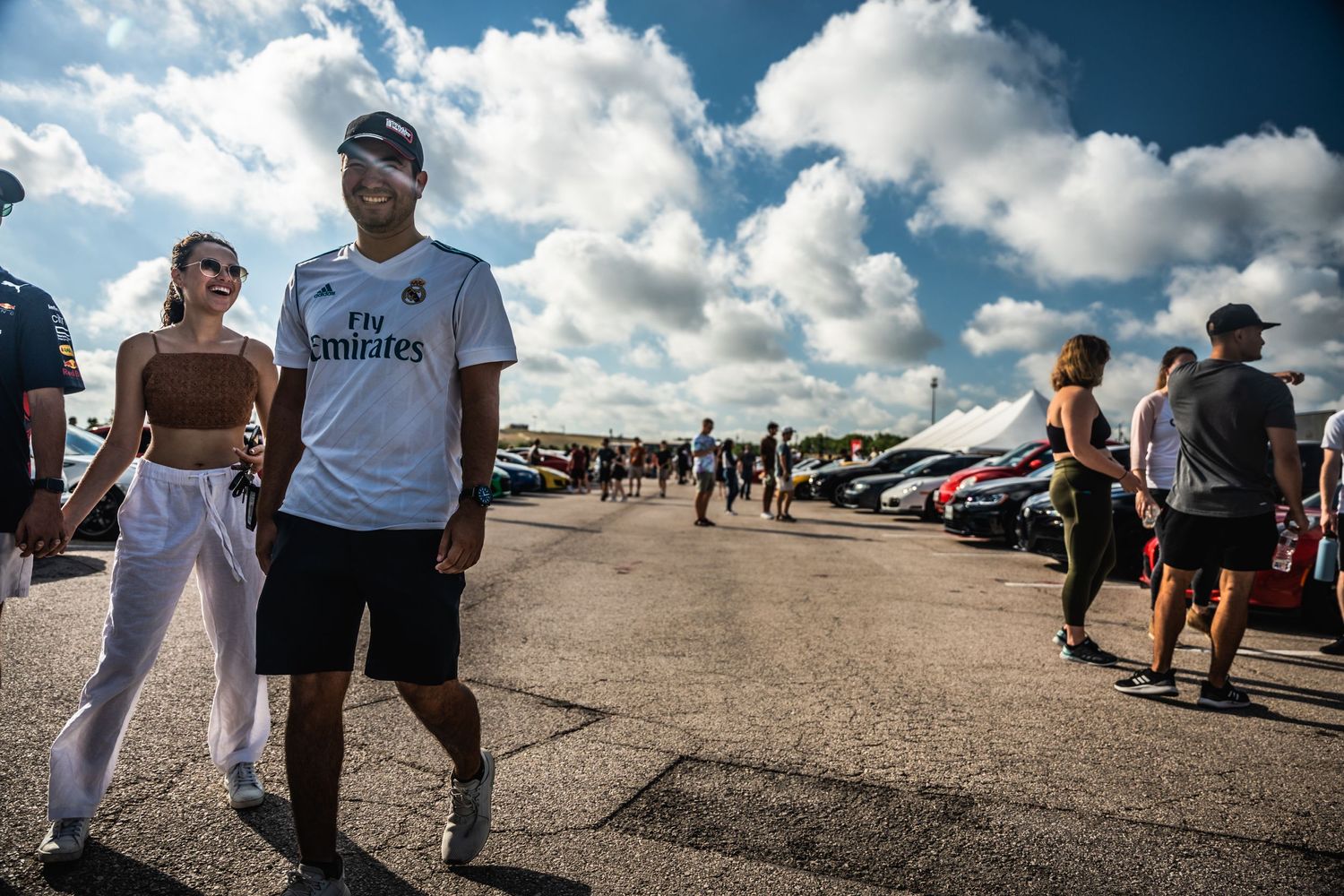 Car enthusiasts gathering at an outdoor automotive event under blue skies.