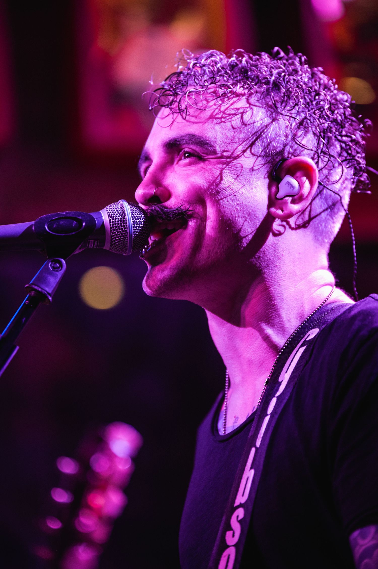 A performer singing passionately into a microphone under purple stage lighting.