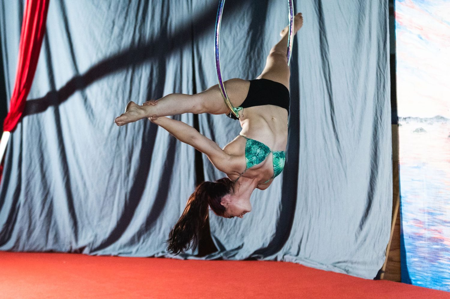Aerialist in black attire performs graceful inverted position on aerial apparatus.