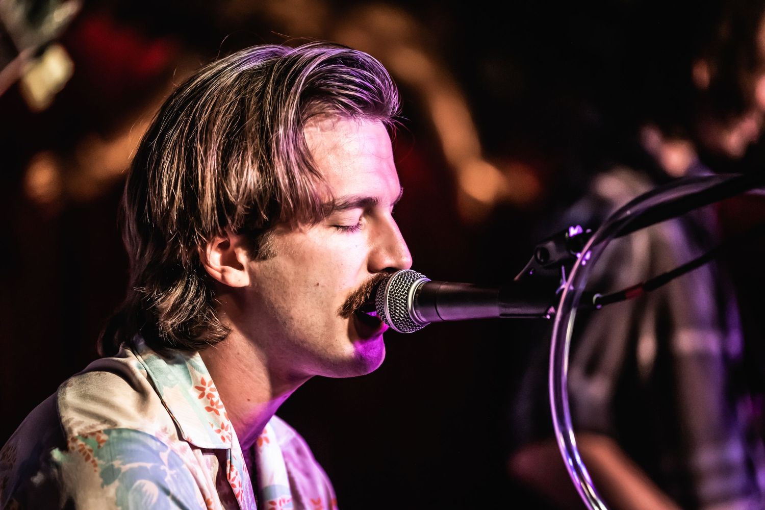 Musician performing live on stage with purple lighting effects.