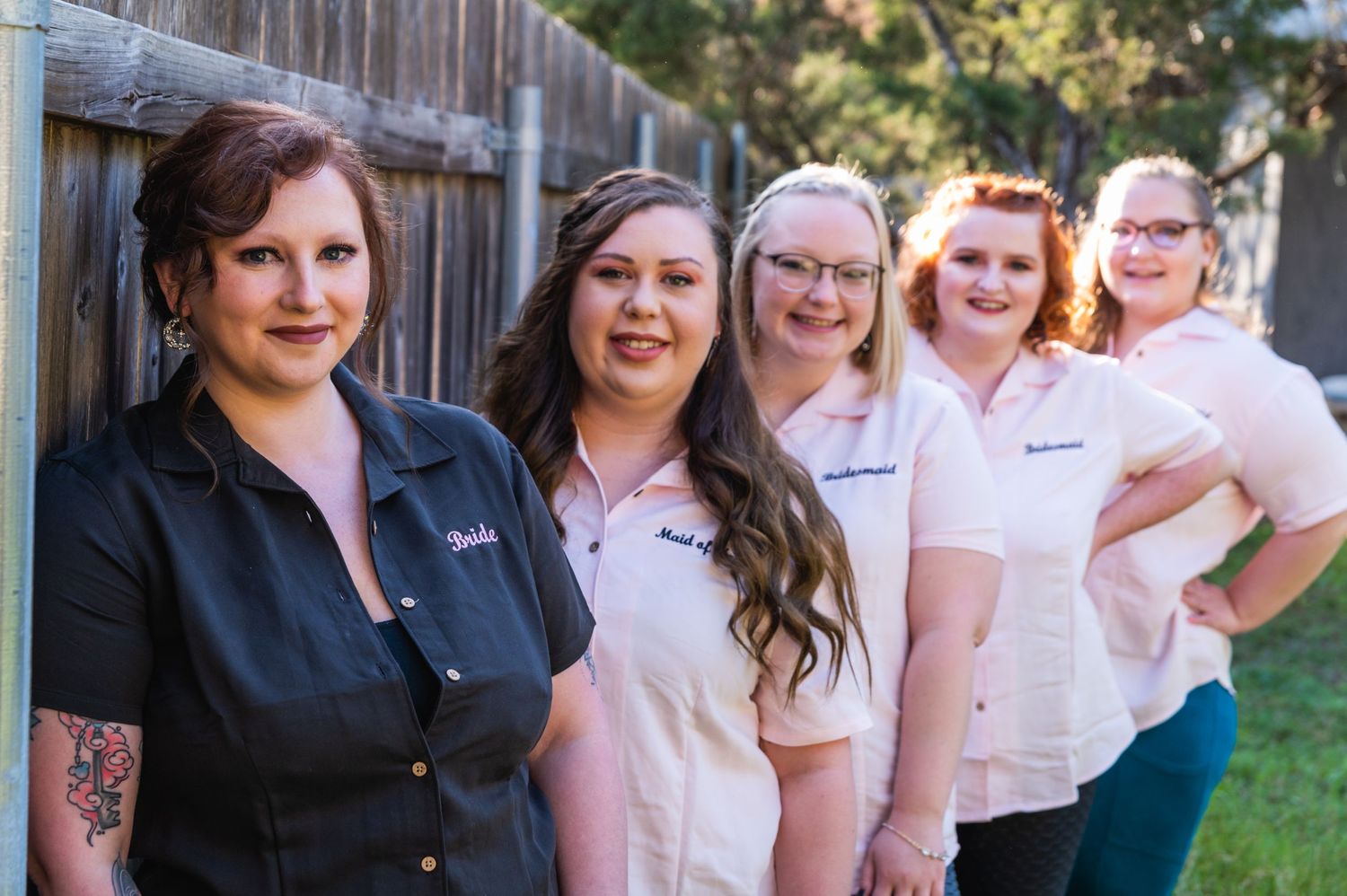 Business team lined up against wooden fence wearing coordinated uniforms.
