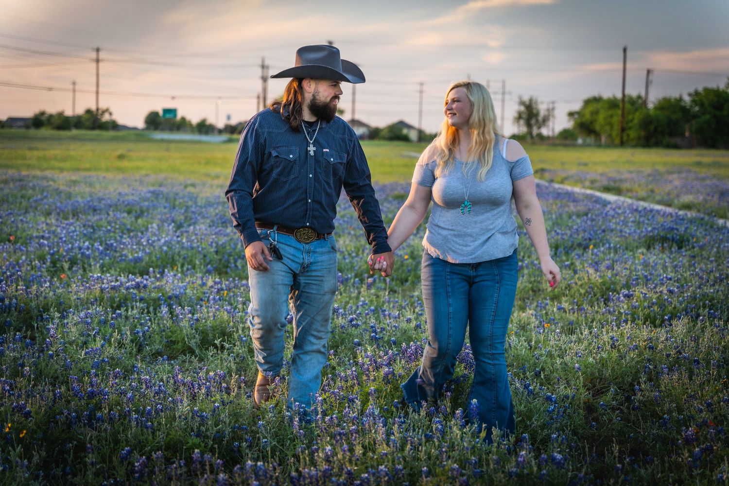 Couple walking through field of bluebonnets at sunset in countryside.