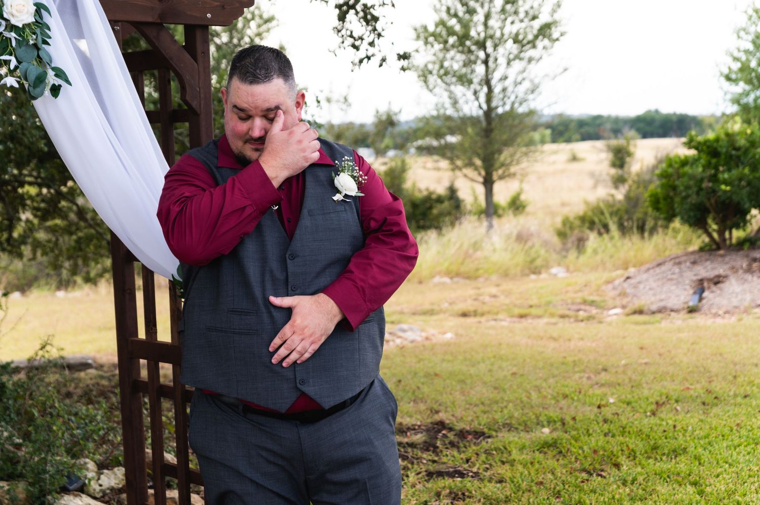 An emotional moment captured as someone wipes tears while standing under a decorated wedding arch.