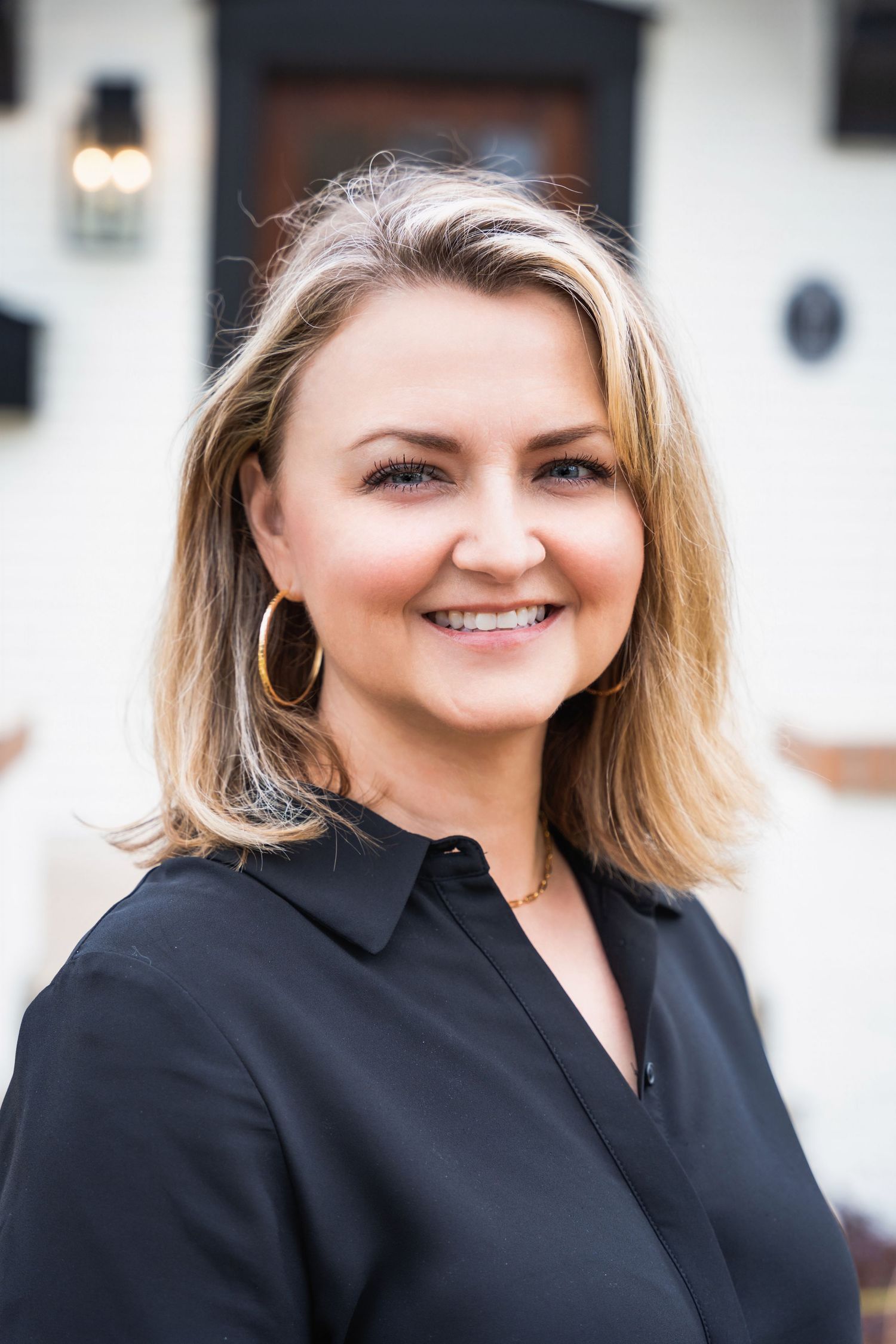 Professional outdoor portrait of person in black button-down shirt with gold hoop earrings.