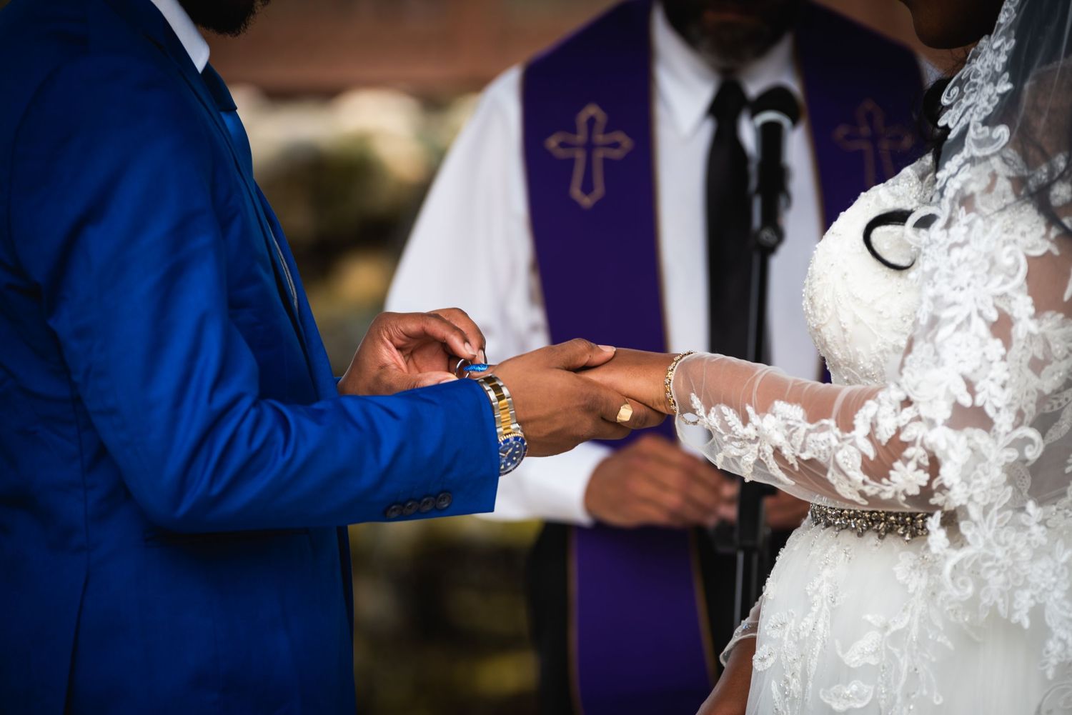 Close-up of ring exchange during wedding ceremony with officiant in purple stole.